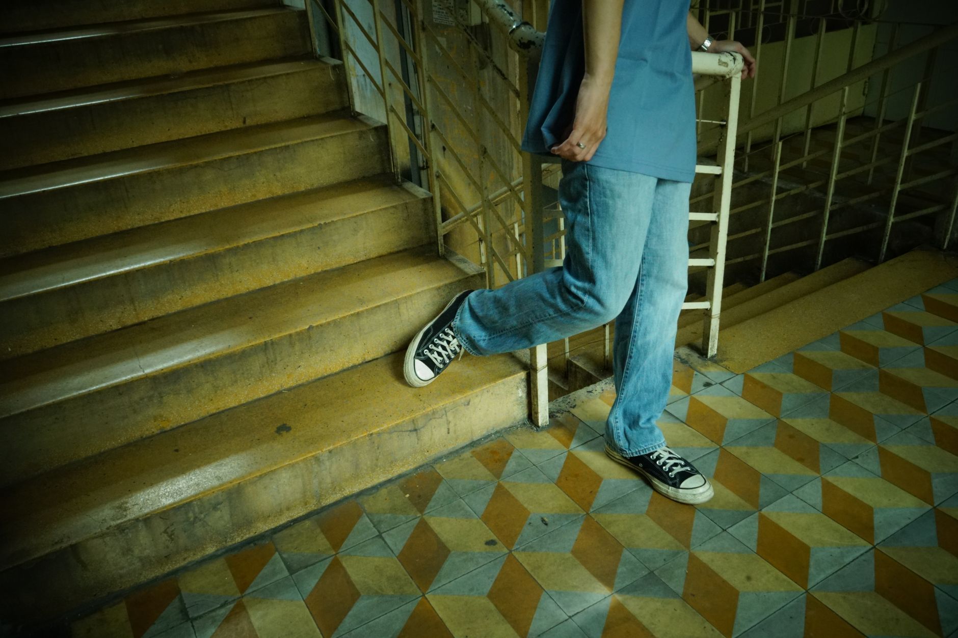 A person in jeans and canvas sneakers caught mid-stride stepping onto a staircase, lower body and walking shoes in focus &mdash; everyday walking, the activity behind the step-count research