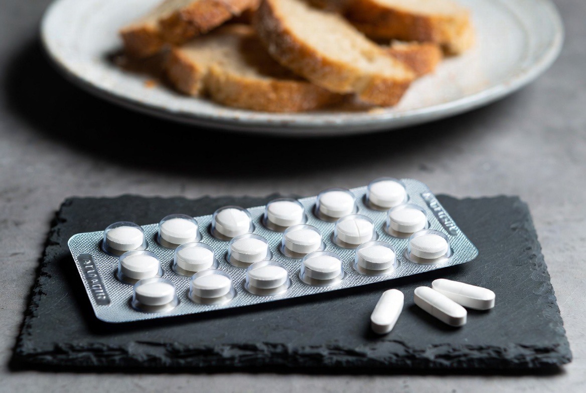 A foil blister pack of round white acarbose tablets resting on a glucose-curve printout, lit like a clinical product still life