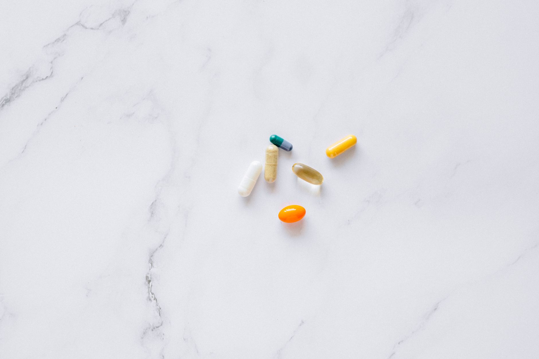 An assortment of plain unbranded supplement capsules and softgels on a clean white marble surface &mdash; alpha-GPC is sold as a daily focus and memory capsule