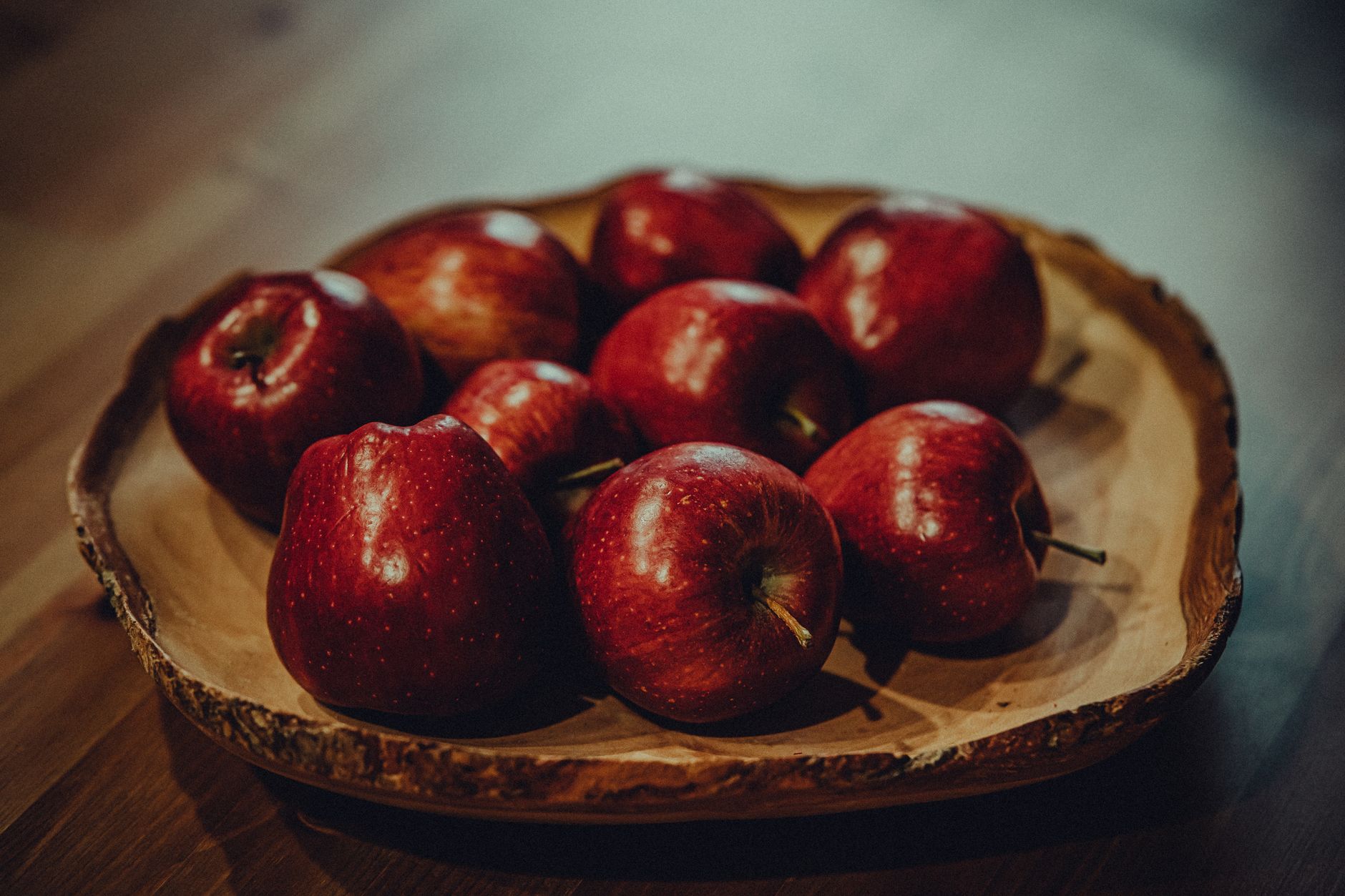 A wooden bowl of fresh red apples on a wooden table in soft natural light — apples are the raw material fermented into apple cider vinegar
