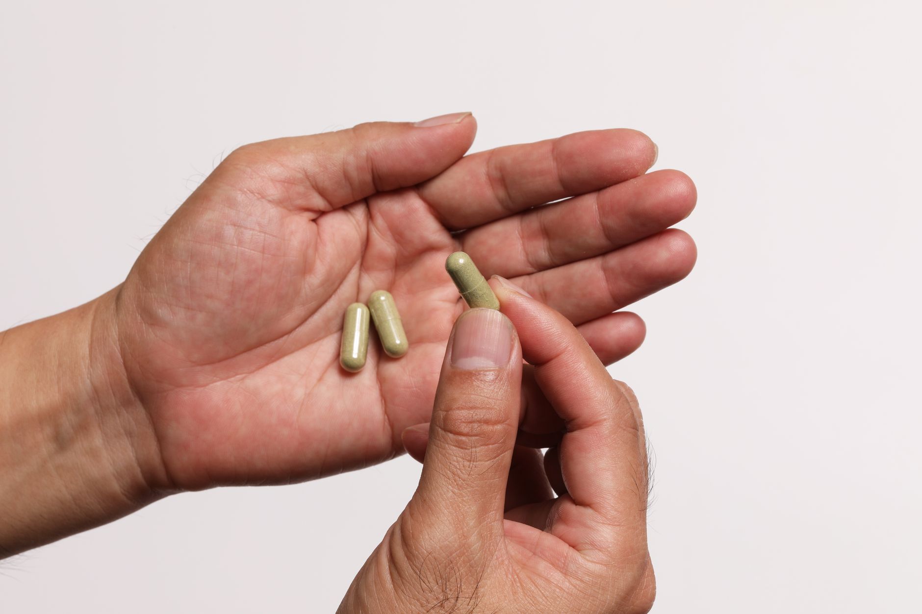 A person holding several olive-green herbal supplement capsules in an open palm against a plain light background