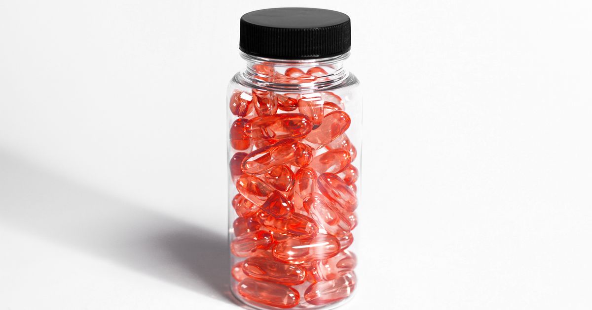A clear supplement bottle filled with translucent deep-red softgel capsules on a clean white background, representing astaxanthin softgels