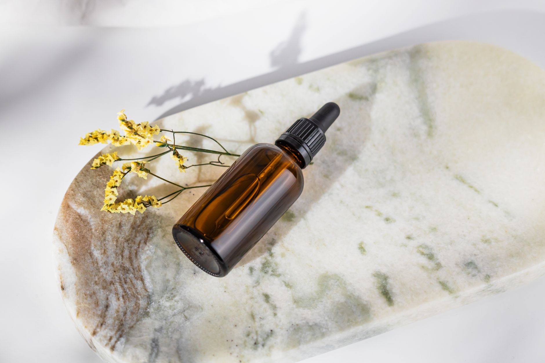 An amber glass serum dropper bottle beside a fresh green botanical leaf on a clean counter in soft daylight &mdash; the plant-derived aesthetic bakuchiol is marketed with