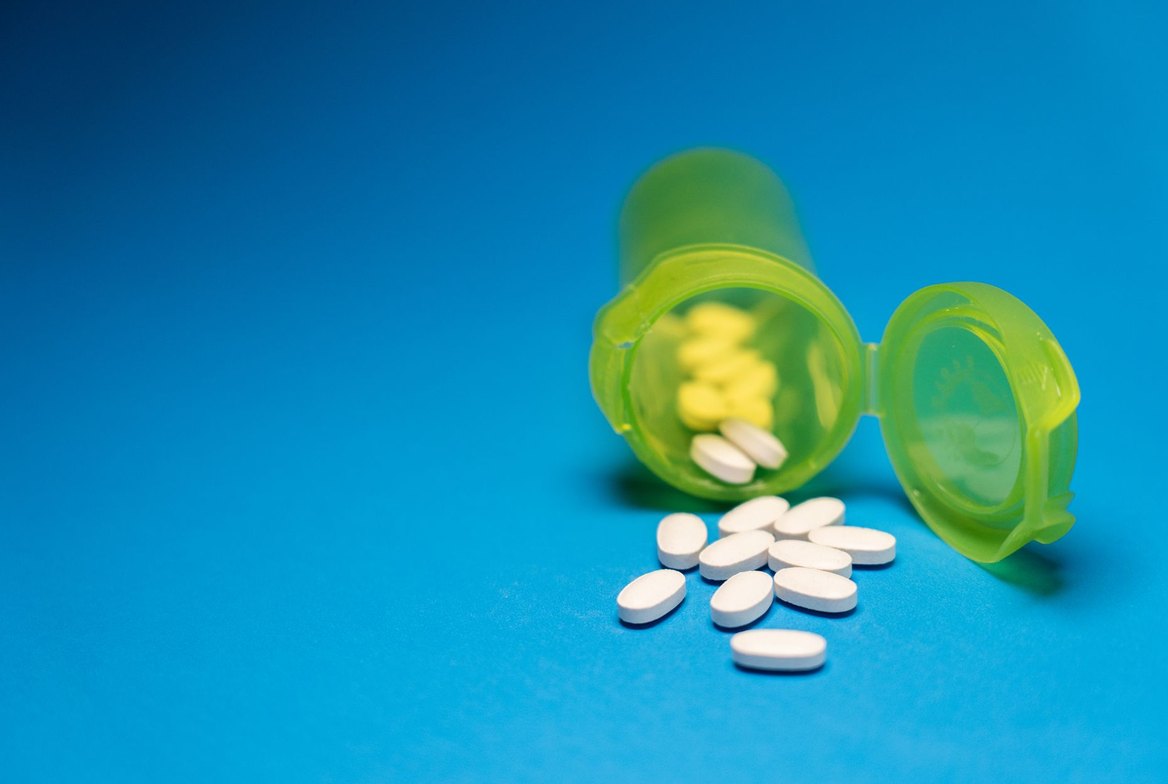 A pill bottle tipped on its side spilling white oral tablets across a surface, illustrating bempedoic acid as a once-daily oral cholesterol-lowering pill rather than an injection