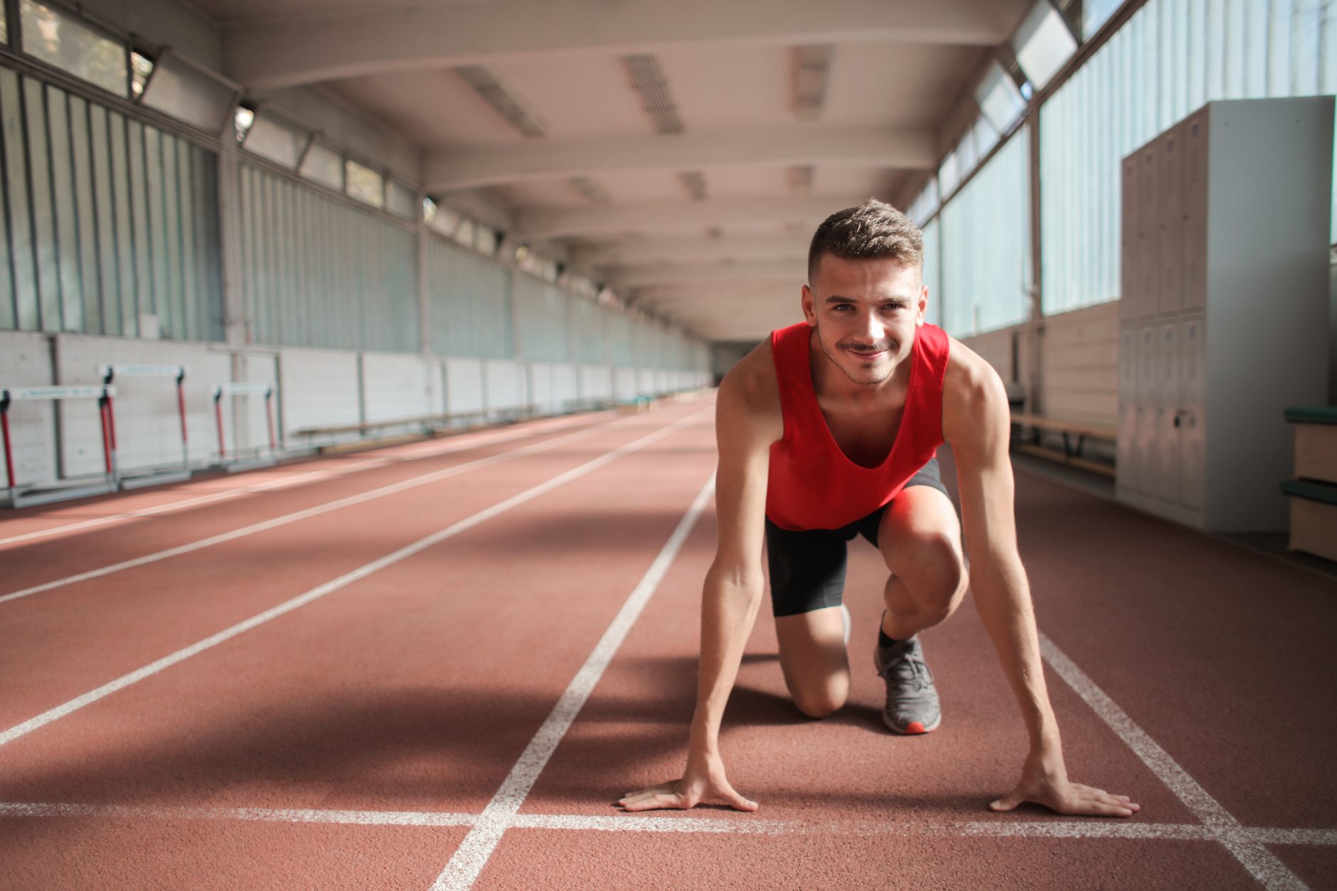 A sprinter set in the starting position on an indoor running track, braced for a hard maximal effort — the kind of one-to-four-minute high-intensity work where beta-alanine's muscle-buffering effect shows up