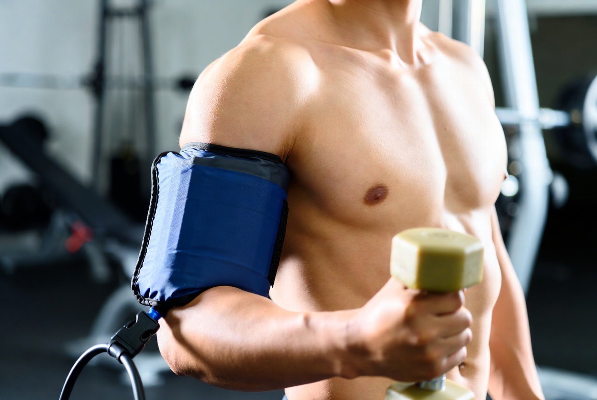 A pneumatic cuff strapped high on a person's upper arm during a light-load blood-flow restriction training set
