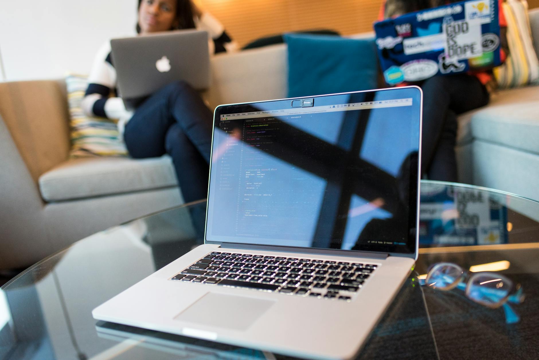 A pair of glasses resting on a desk in front of a glowing laptop screen in a dim evening room