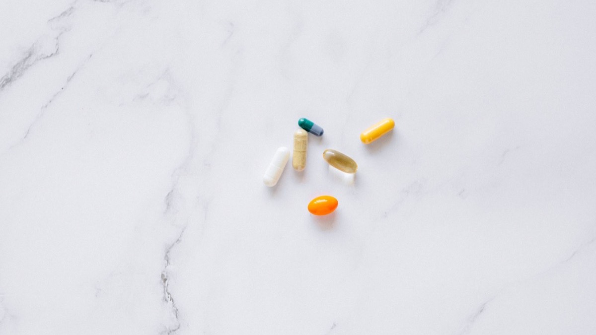 An assortment of capsules and tablets arranged on a clean white marble surface, representing longevity and supplement research