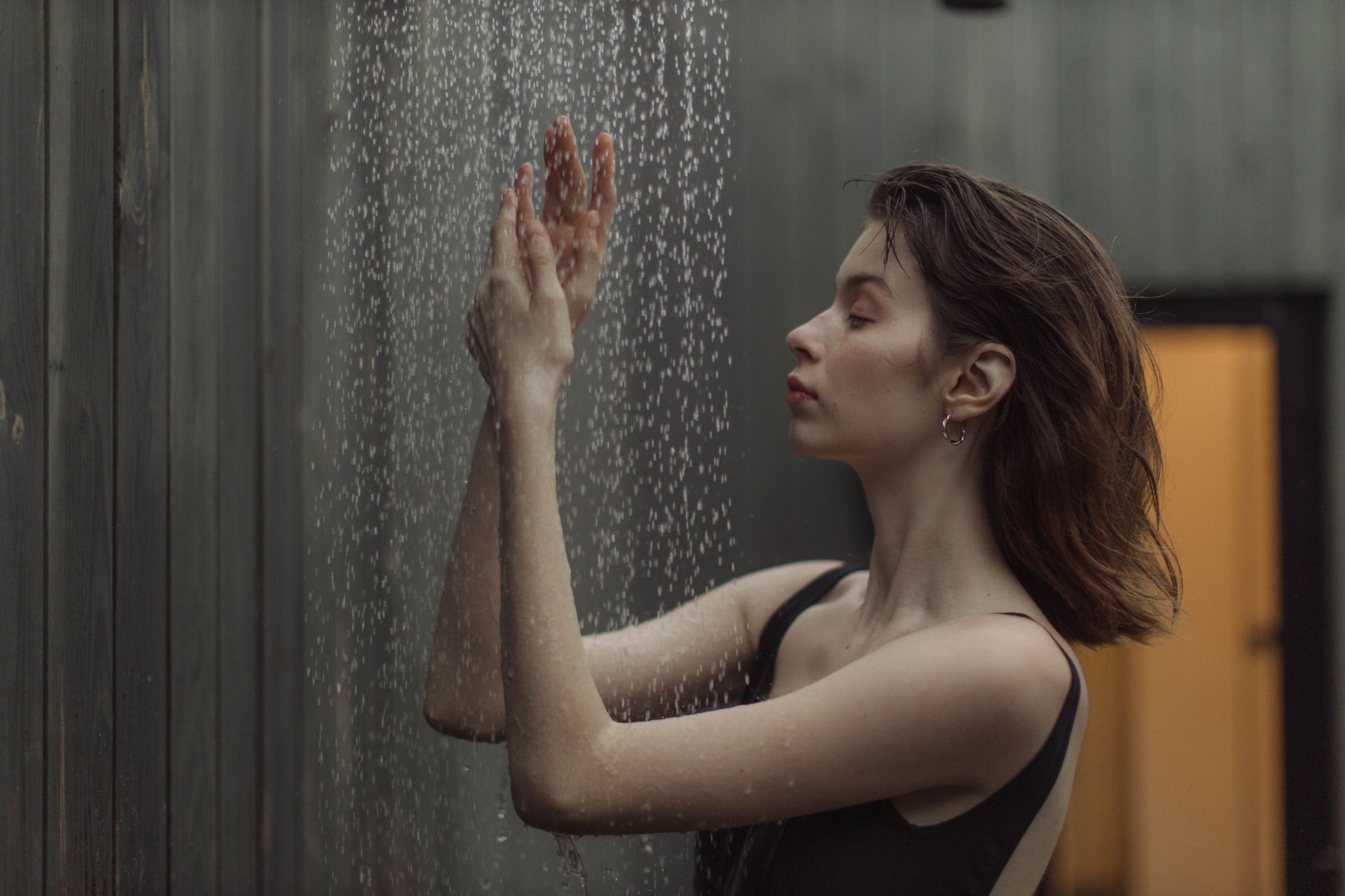 A woman standing under a stream of falling shower water, droplets catching the light as she raises her hands into the spray