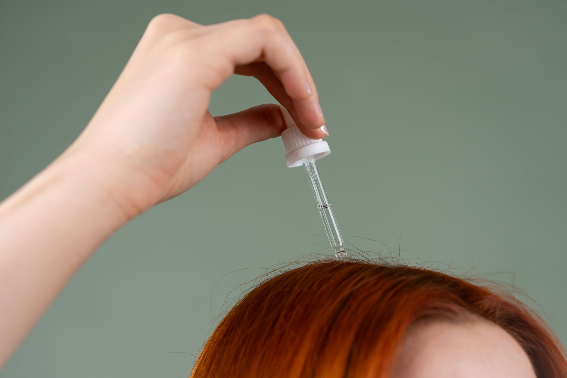 A hand applying a clear serum from a glass dropper directly onto the scalp at the hairline &mdash; the scalp-serum format copper peptides for hair are sold in