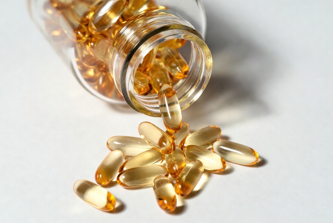 Amber CoQ10 ubiquinol softgel capsules spilling from a supplement bottle onto a light surface, representing the consumer coenzyme Q10 supplement category