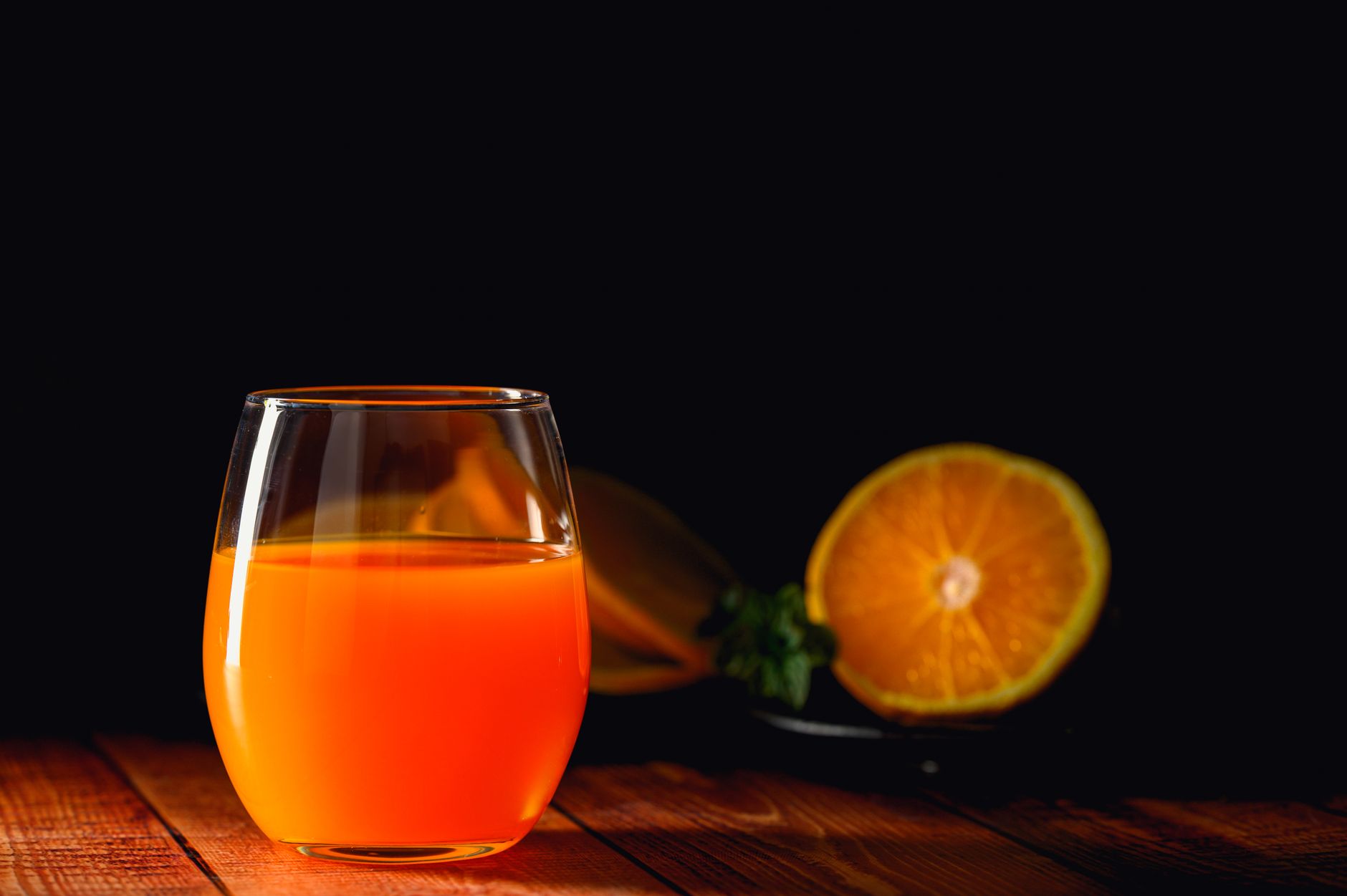 A glass of bright orange citrus juice on a wooden surface beside a halved orange, the kind of orange-based mocktail marketed as a cortisol cocktail