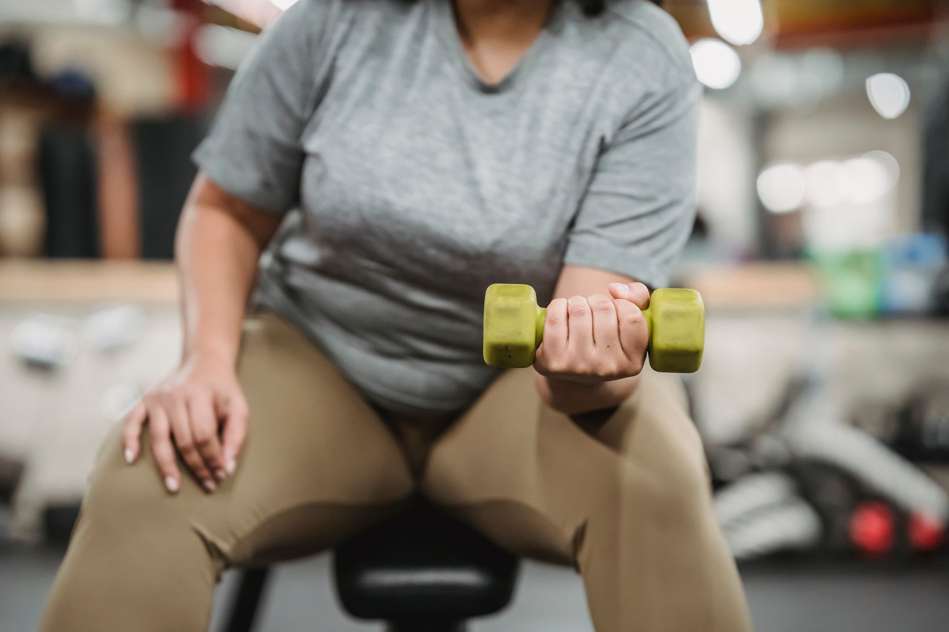 A woman seated on a gym bench performing a dumbbell curl during resistance training, representing strength training that creatine supplementation supports in women