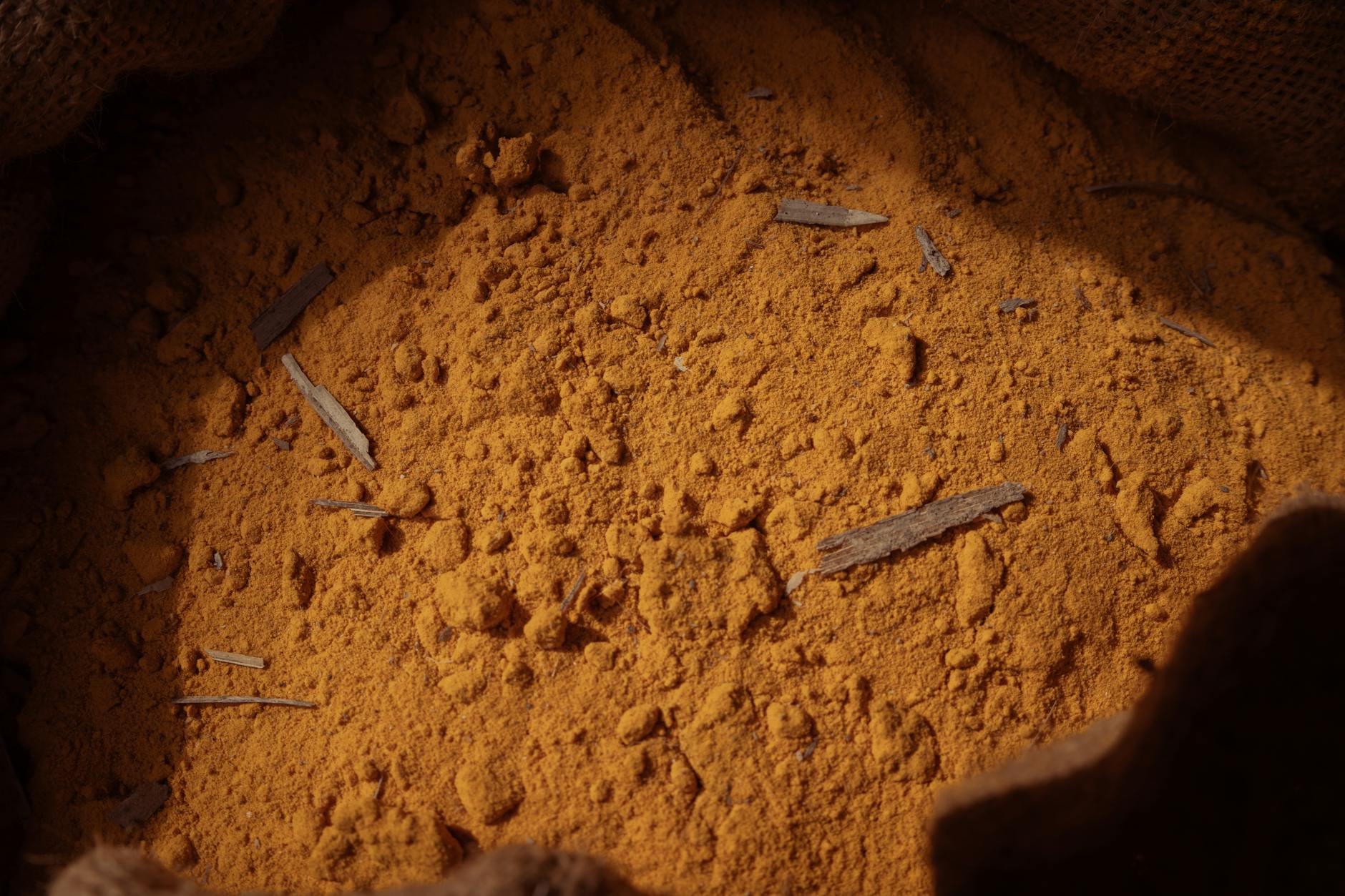 Golden-orange turmeric (curcumin) powder in a coarse burlap sack with a few small stick fragments, lit by warm natural light