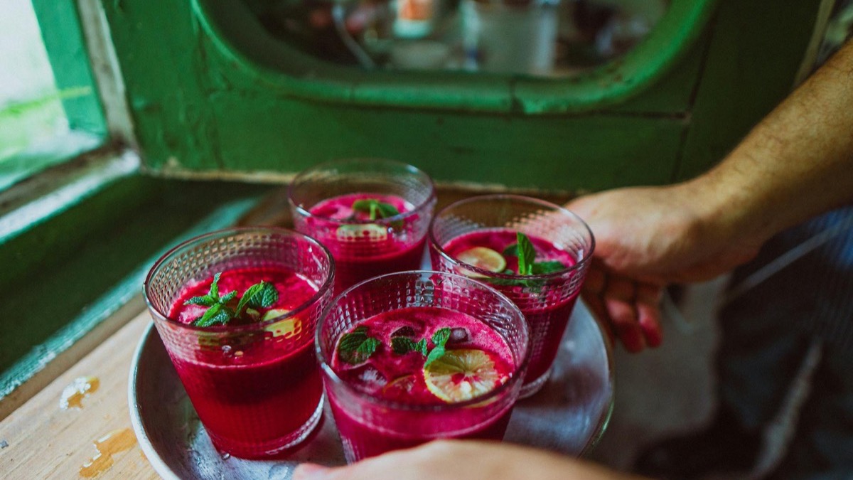 Four glasses of deep red beetroot juice garnished with mint and lime, served on a tray — dietary nitrate from beetroot is the source of its endurance effect