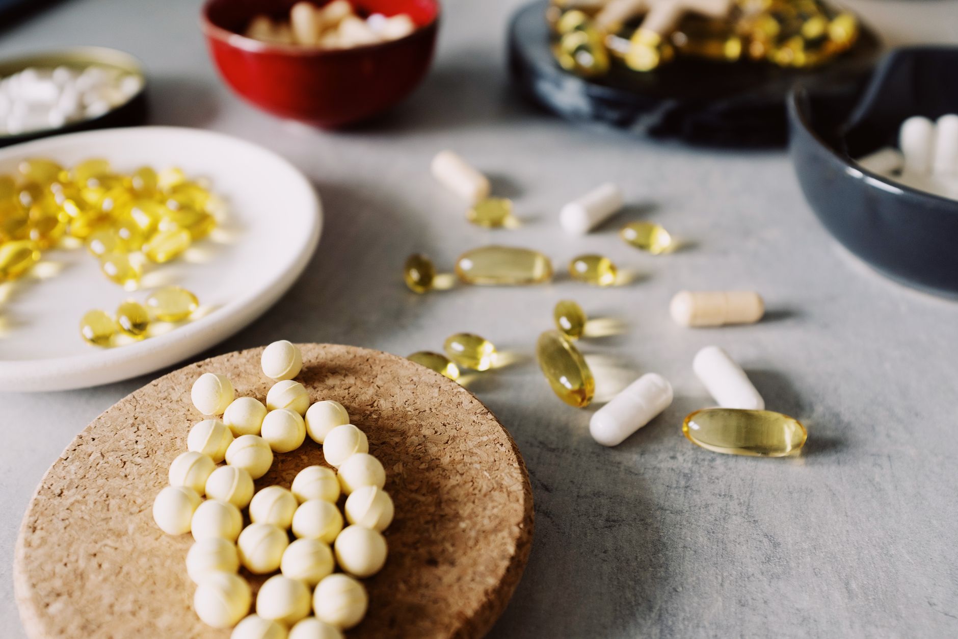 An assortment of over-the-counter supplement capsules, tablets, and amber softgels scattered across a grey kitchen surface and small dishes — the broad category of digestive enzyme and supplement products sold for digestion