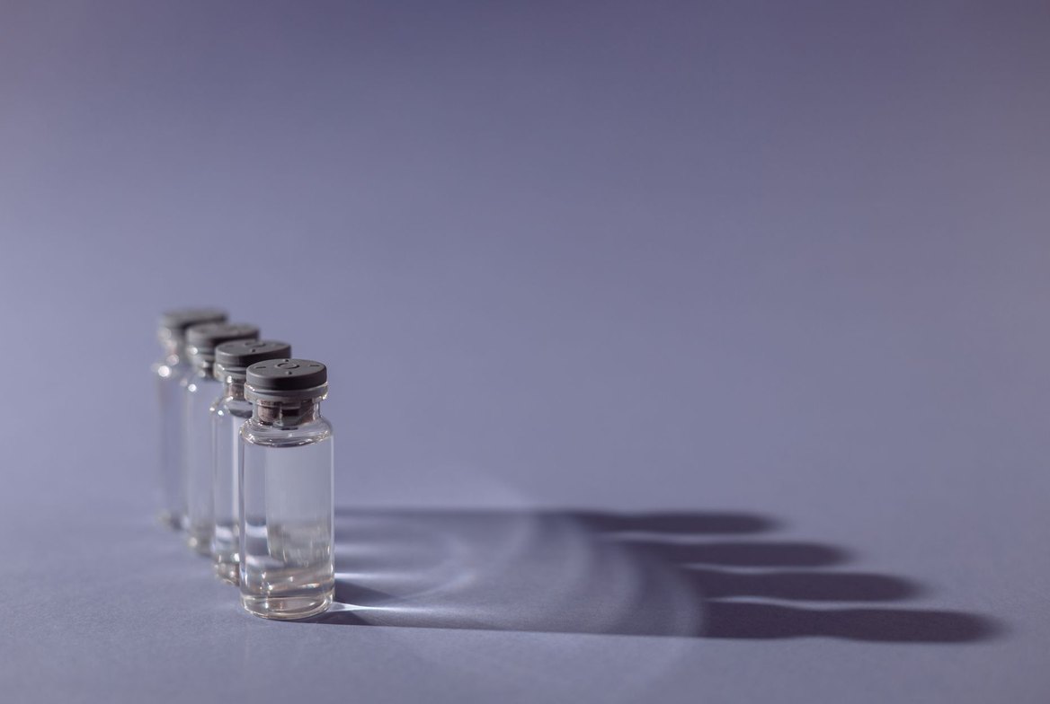 A row of small clear glass medical vials with grey crimp caps on a calm grey-lavender surface, softly lit &mdash; representing DSIP, the injectable research peptide sold as reconstitutable vials and marketed for sleep and recovery