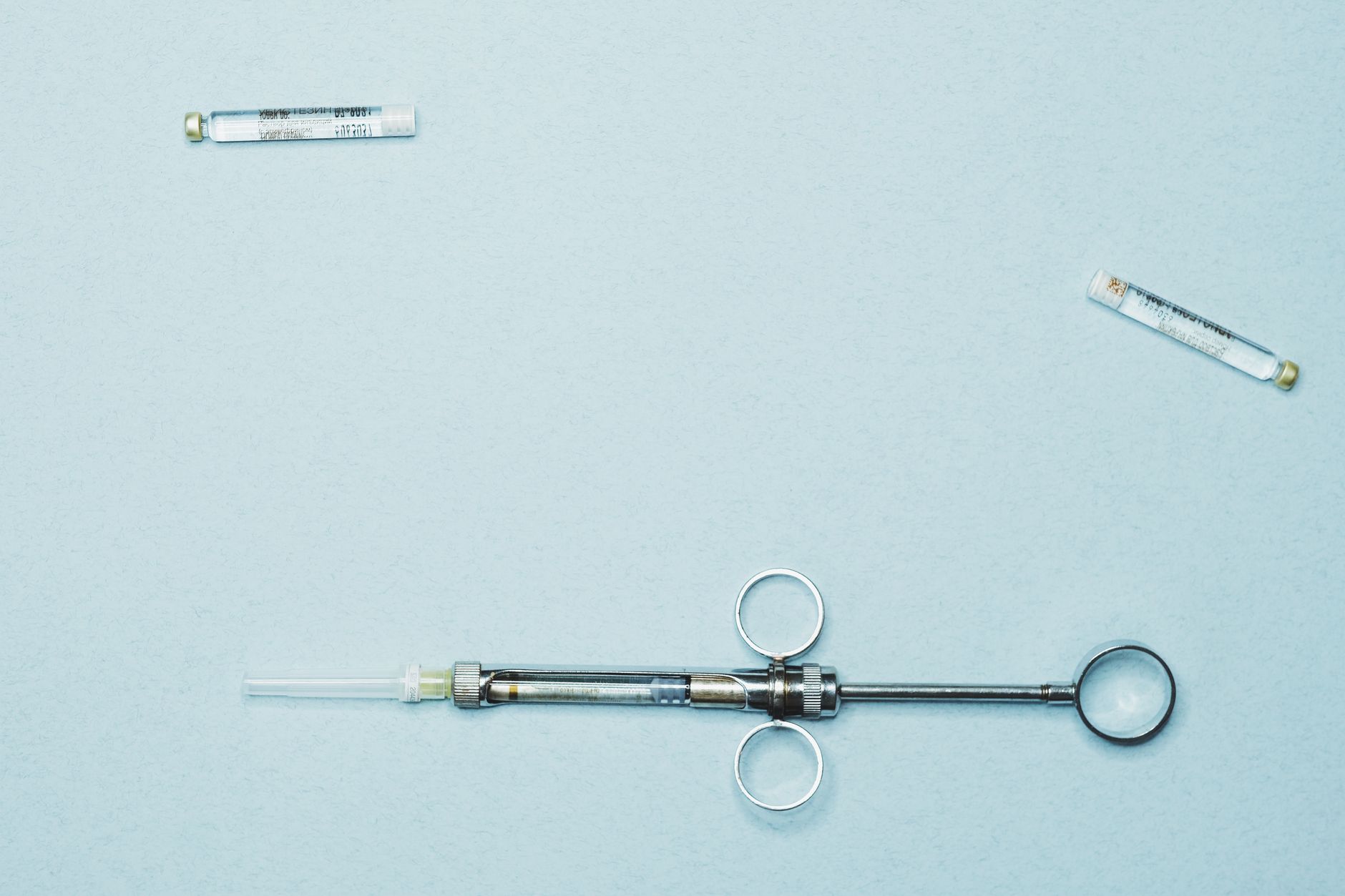 Two sealed glass peptide ampoules and an injection device on a clean clinical-blue surface — research-peptide and injectable context