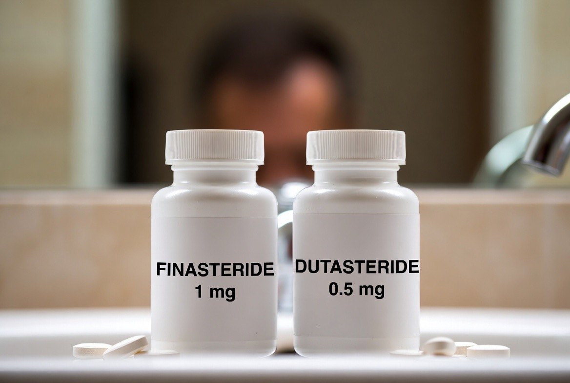 Two prescription tablet bottles of oral hair-loss medication side by side on a bathroom counter, with a man examining his receding hairline in the mirror behind them