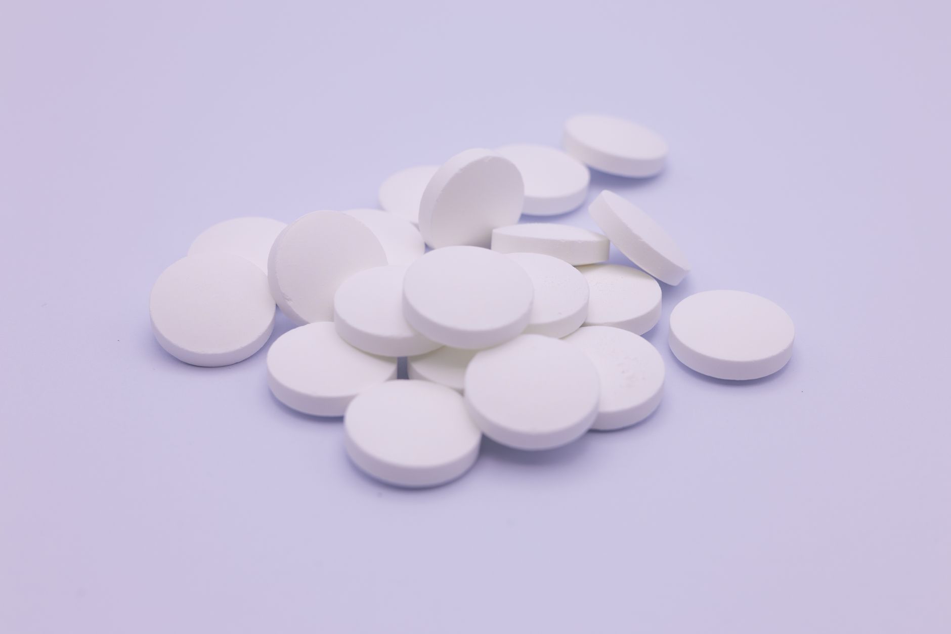 A loose pile of plain round white supplement tablets on a soft pale neutral background, representing a generic joint-health pill like glucosamine