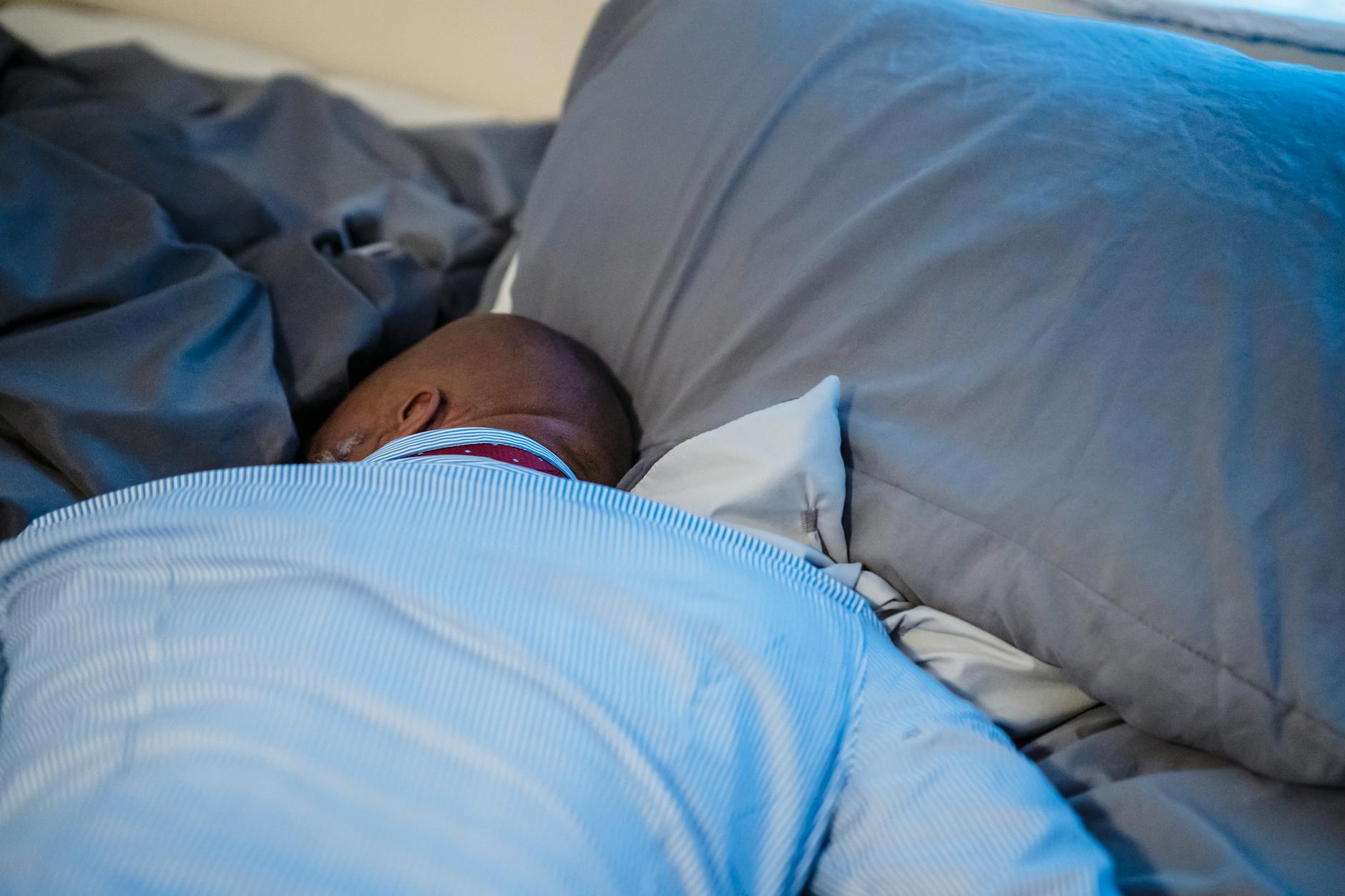 A person sleeping peacefully under a blanket in a dim, calm bedroom at night — glycine works by easing the body into the cooling state that precedes sleep
