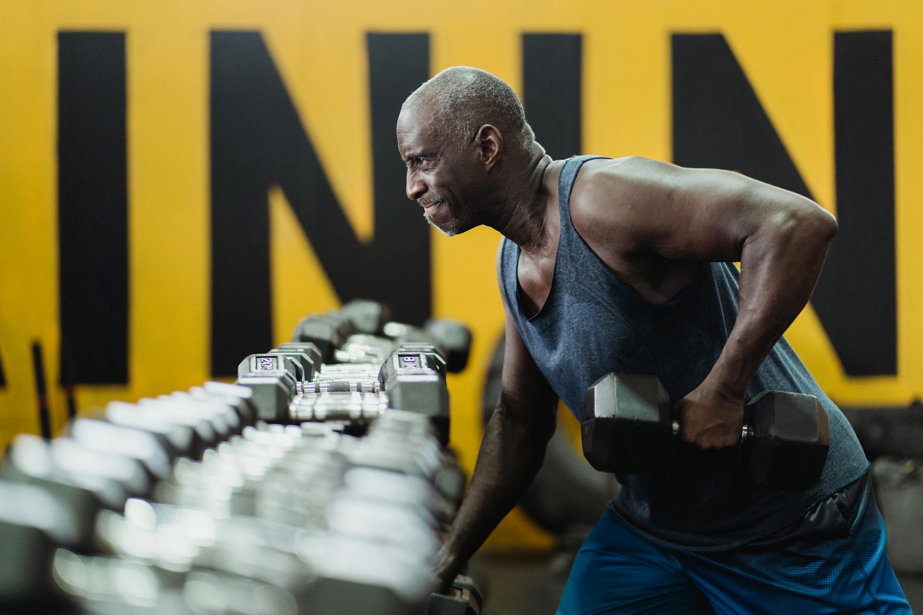 Older adult performing a dumbbell biceps curl in a well-lit gym, focused expression