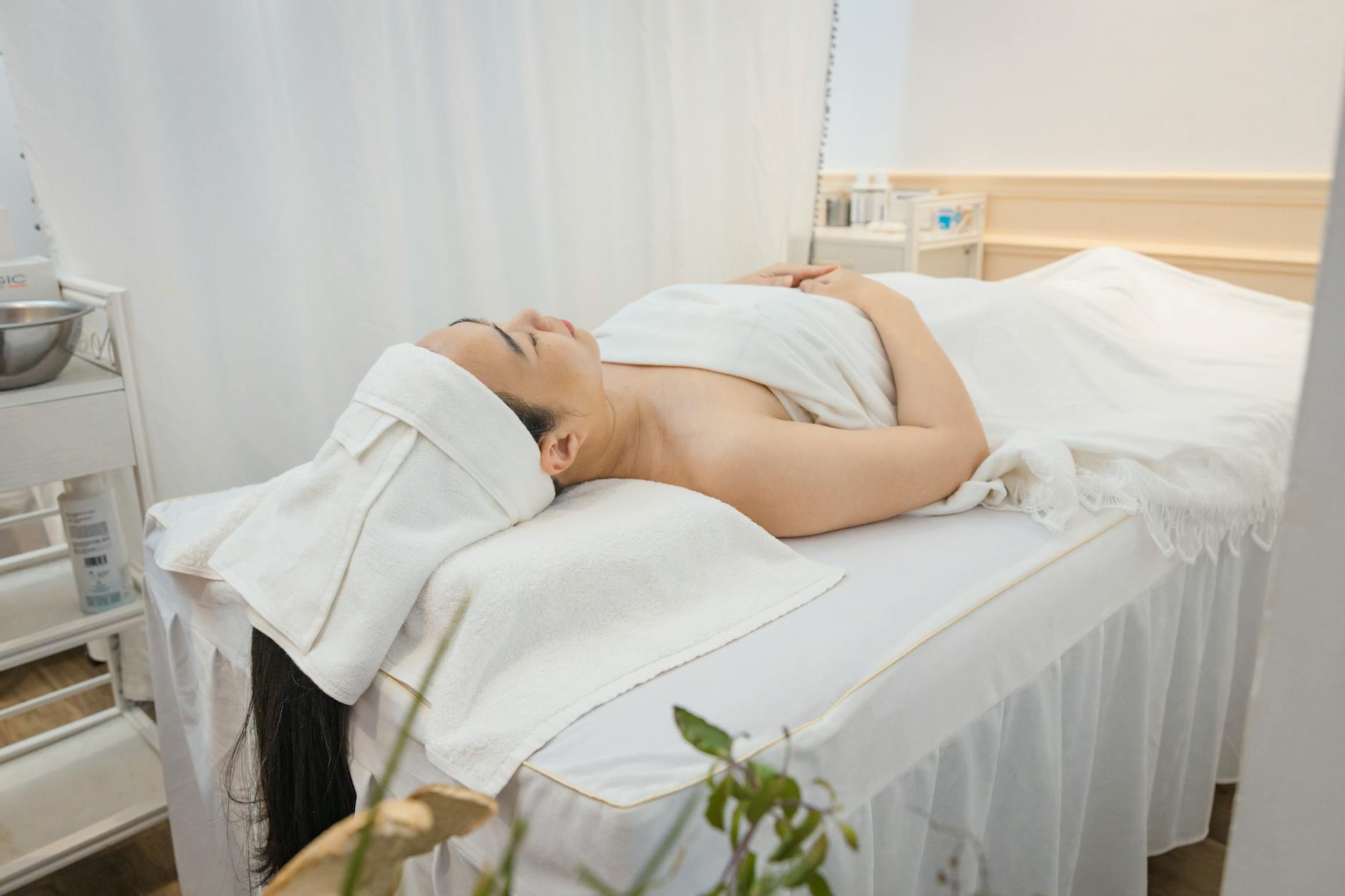 A person lying wrapped in towels and a sheet on a spa treatment table in a calm, light-filled room, representing a passive lying-down heat-and-relaxation session