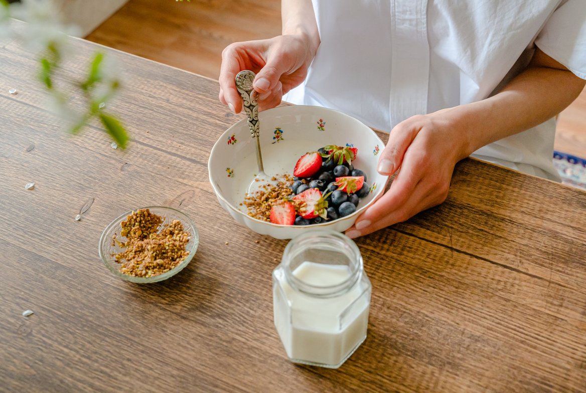 A glass jar of milk on a wooden table beside a bowl of yogurt topped with fresh berries and granola, the dairy foods at the center of the milk-health debate