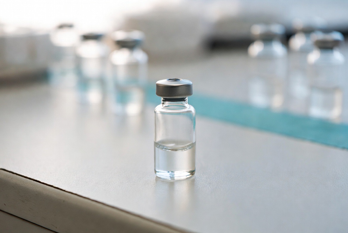 A single clear glass research peptide vial with a rubber-stopper cap resting on a stainless laboratory surface under soft clinical light