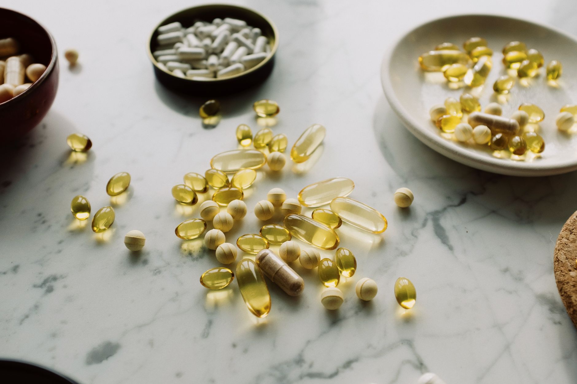 L-carnitine supplement capsules and softgels scattered across a marble surface beside small bowls, representing the consumer fat-burner supplement category