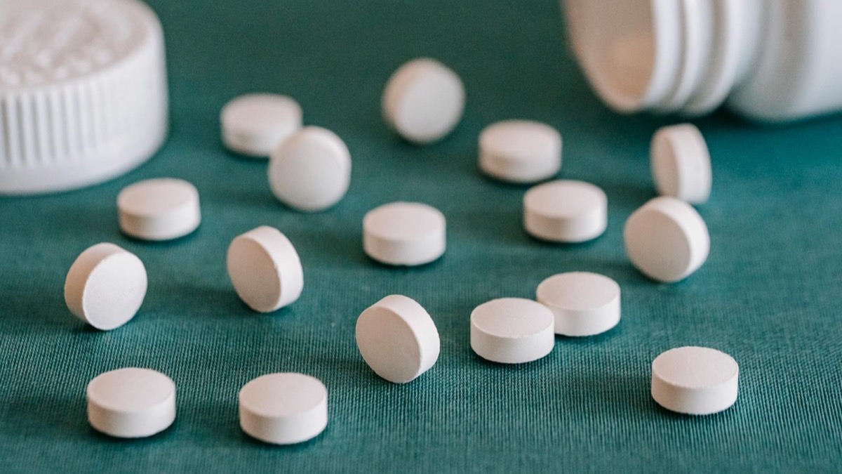 White supplement capsules and tablets spilling from an open bottle onto a pale neutral surface — magnesium is sold in many different chemical forms