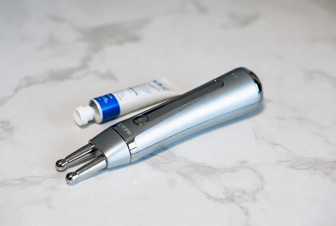A handheld microcurrent facial device with two metal sphere probes resting on a clean white vanity