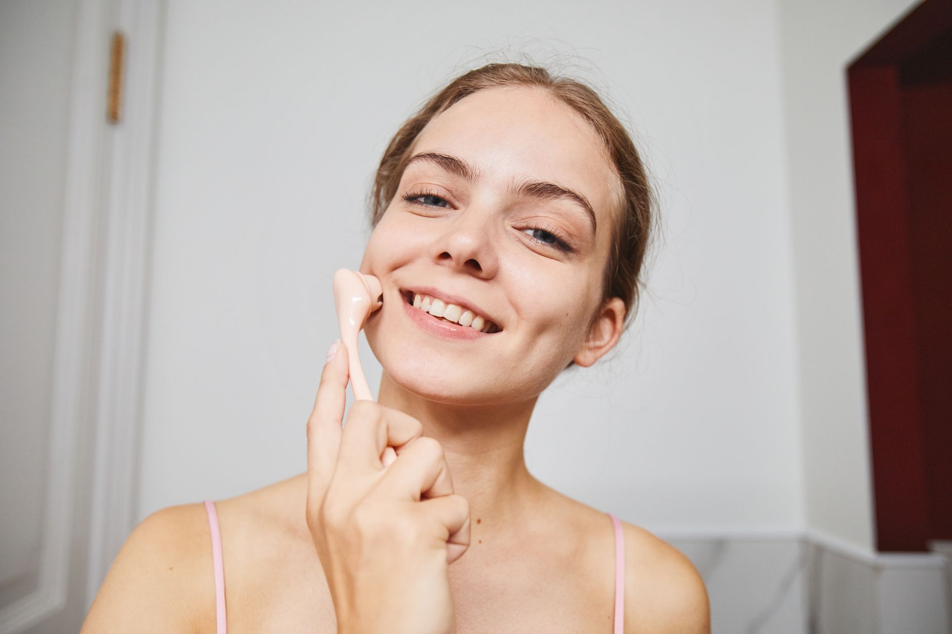 A person rolling a handheld at-home derma-roller skincare device across their cheek, representing consumer microneedling