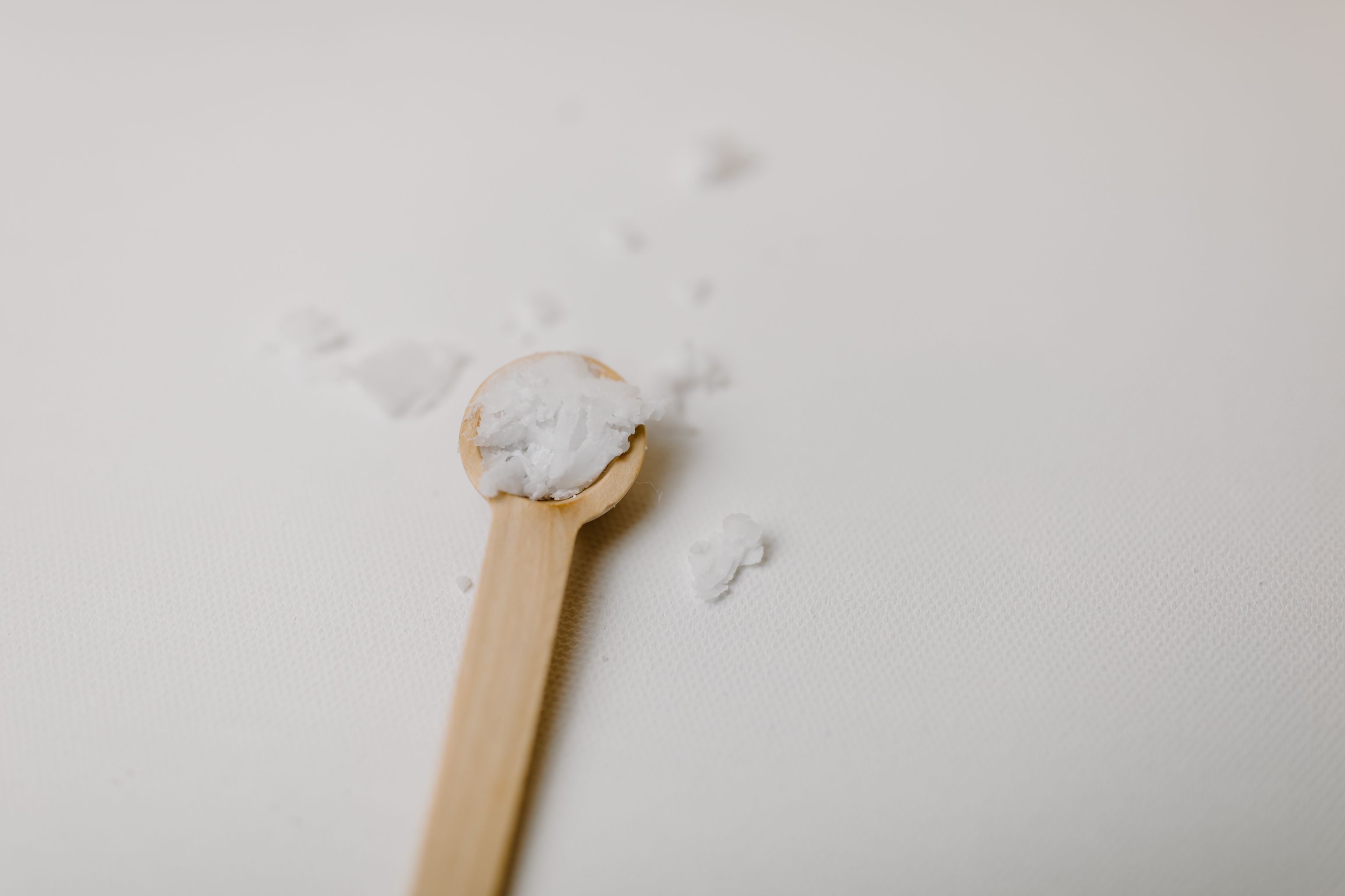 A small wooden scoop of cream-white collagen peptide powder spilled on a bright white surface