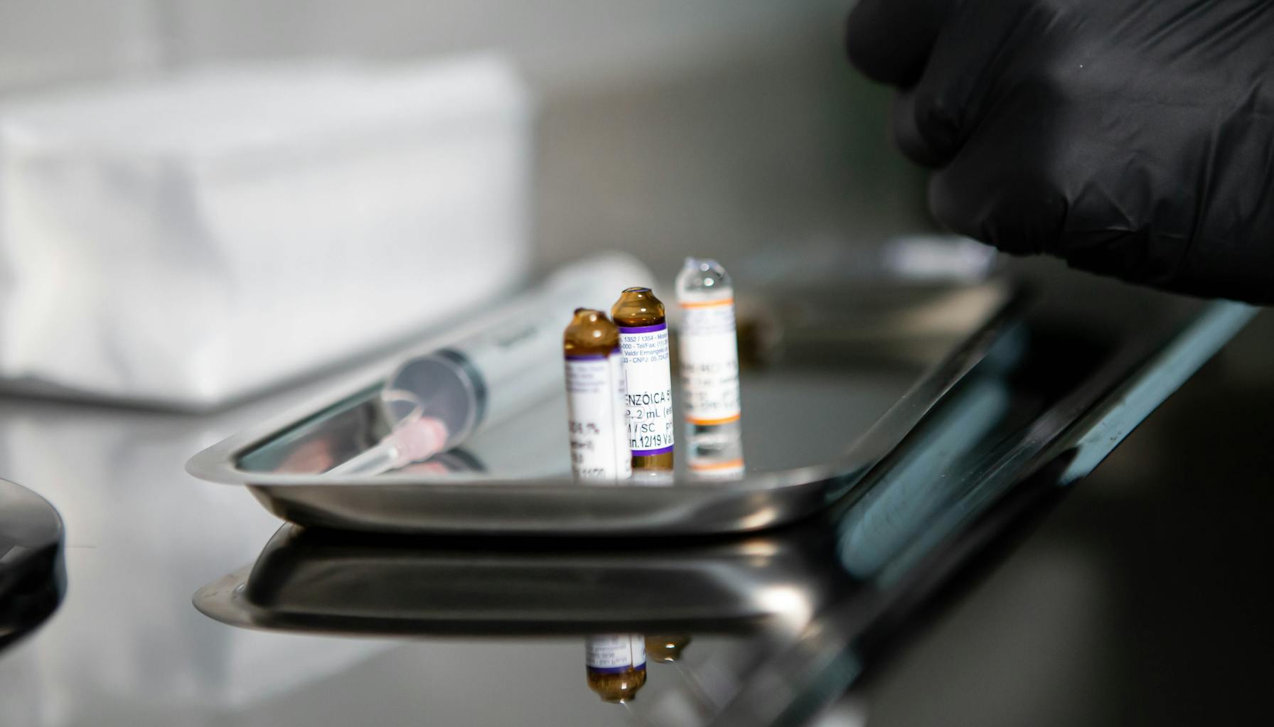 Several unlabeled glass peptide vials and a syringe on a stainless steel surface under clinical light