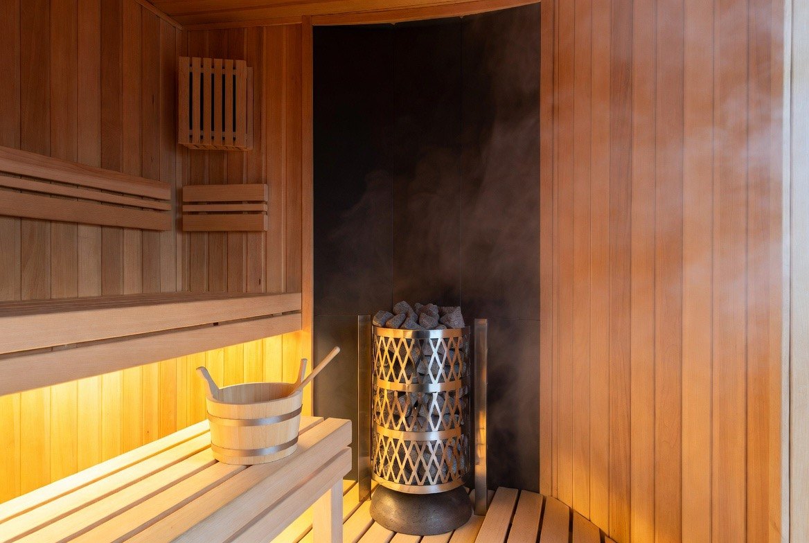 The warm wood-panelled interior of a traditional Finnish sauna, with a person relaxing on the tiered bench beside a heater piled with hot rocks releasing steam &mdash; the everyday ritual behind the Finnish cardiovascular cohort data