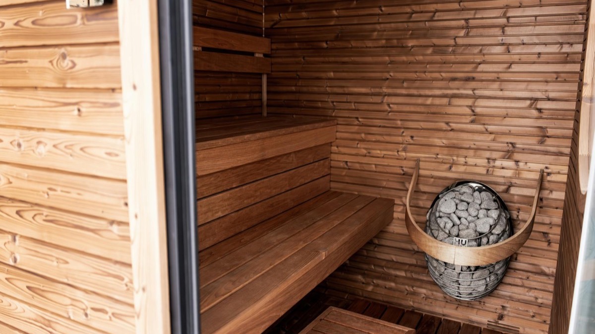Warm wooden sauna interior with timber benches, a stove and heated stones lit by soft natural light — the setting for the heat exposure studied in Finnish cardiovascular research