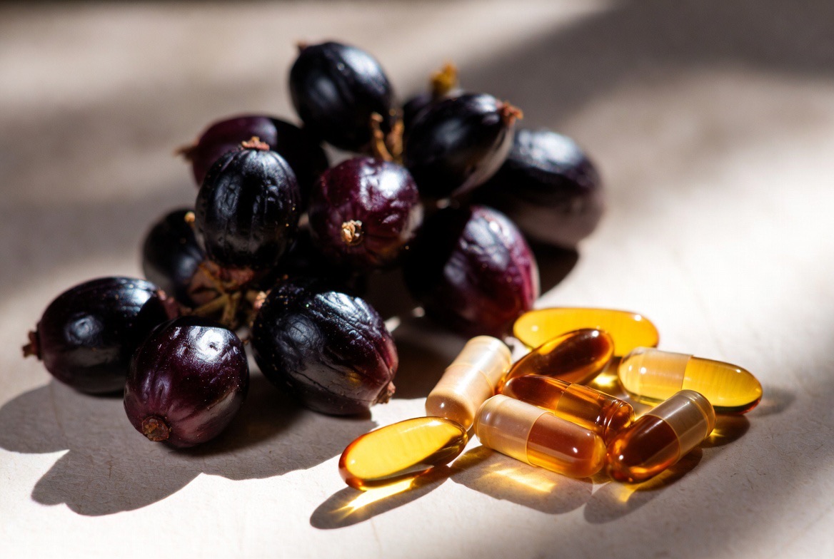 Dark ripe saw palmetto berries beside herbal supplement capsules on a neutral surface