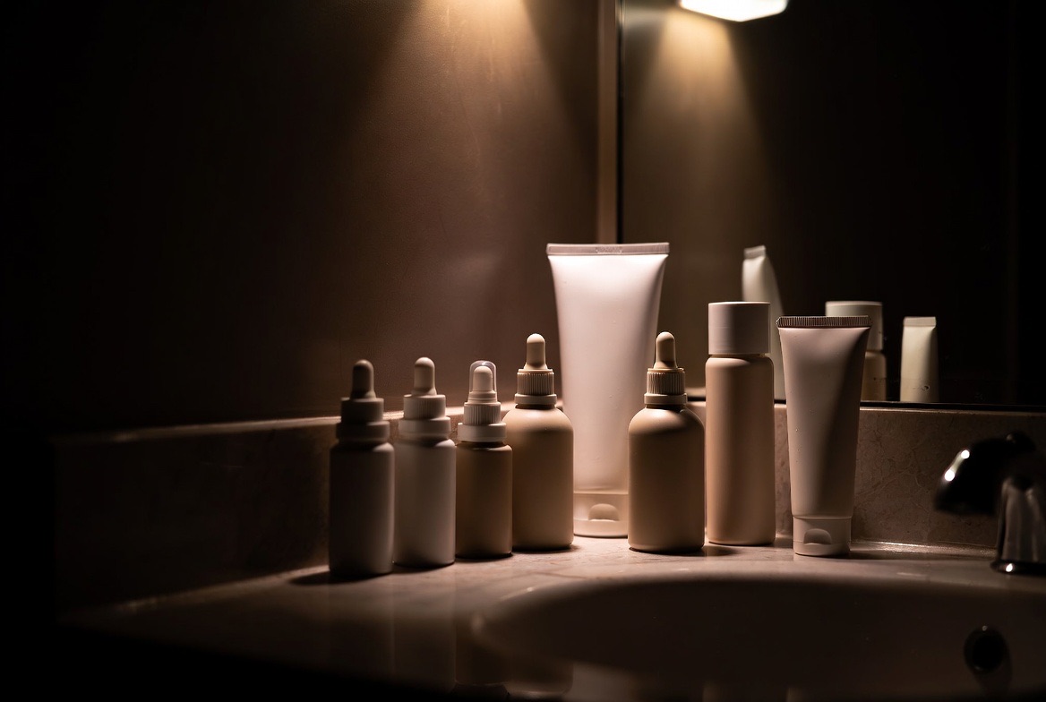 A row of serum and moisturizer bottles arranged on a clean bathroom counter in soft daylight, representing a structured nightly skincare routine