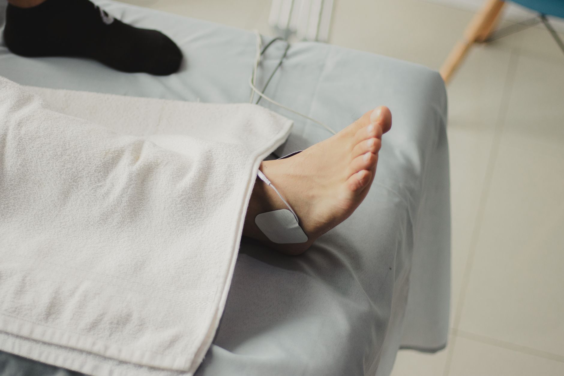 A self-adhesive TENS electrode pad with its lead wire attached to a patient's ankle on a treatment table in a clinic