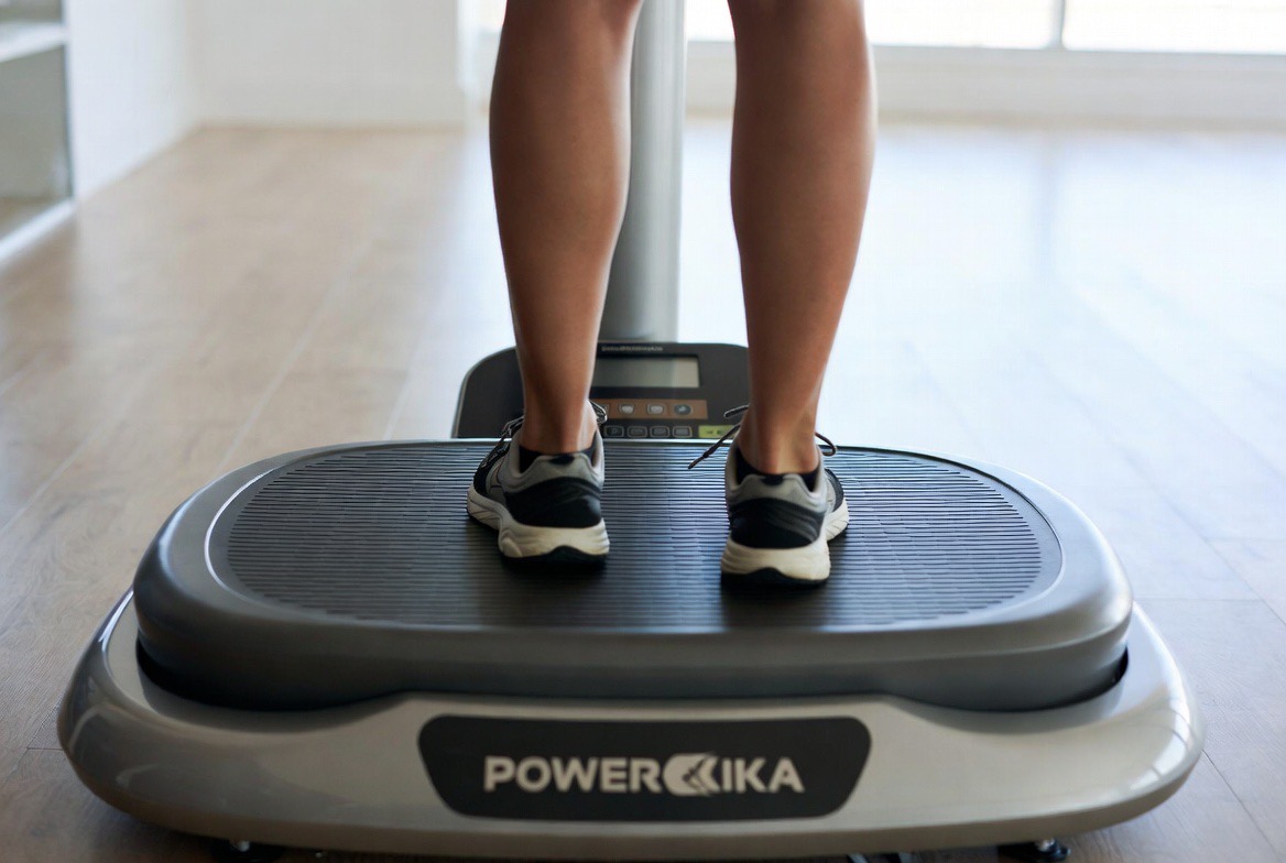 A person standing in a half-squat on a whole-body vibration plate platform in a home gym