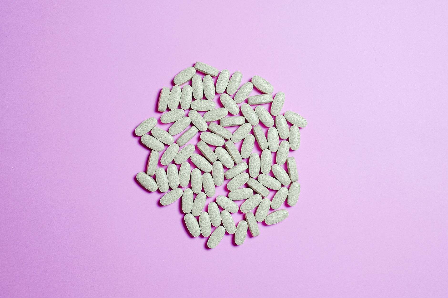 A cluster of pale green-white oblong zinc supplement tablets on a soft pink background