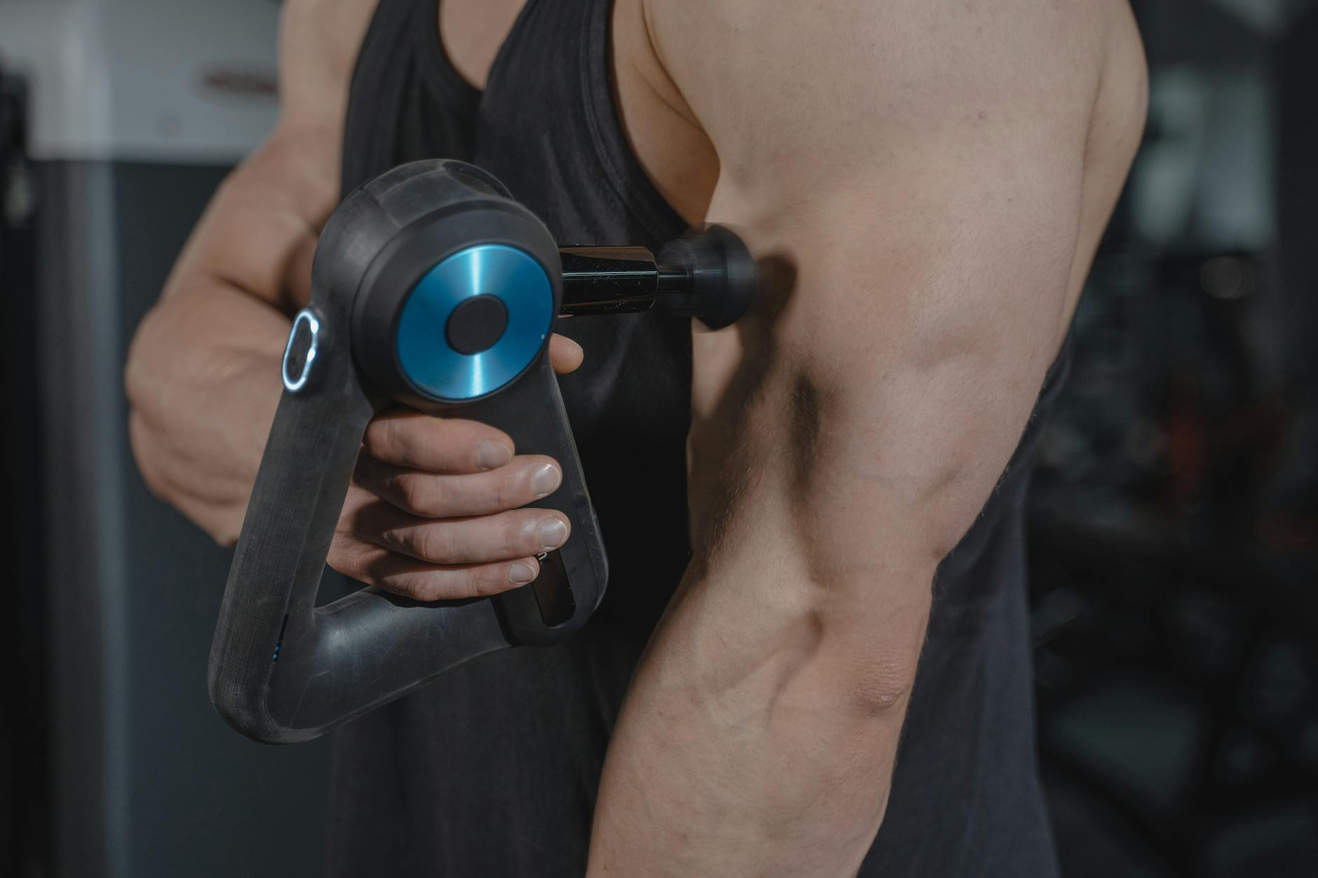 Athlete using a percussive massage gun on a bicep in the gym — recovery and pain